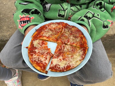 Ein Junge hält seine fertige Pizza in einem Teller auf dem Schoß